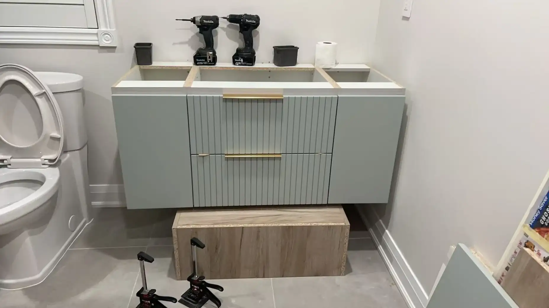 Sage green floating bathroom vanity with fluted drawer fronts and brass pulls being installed