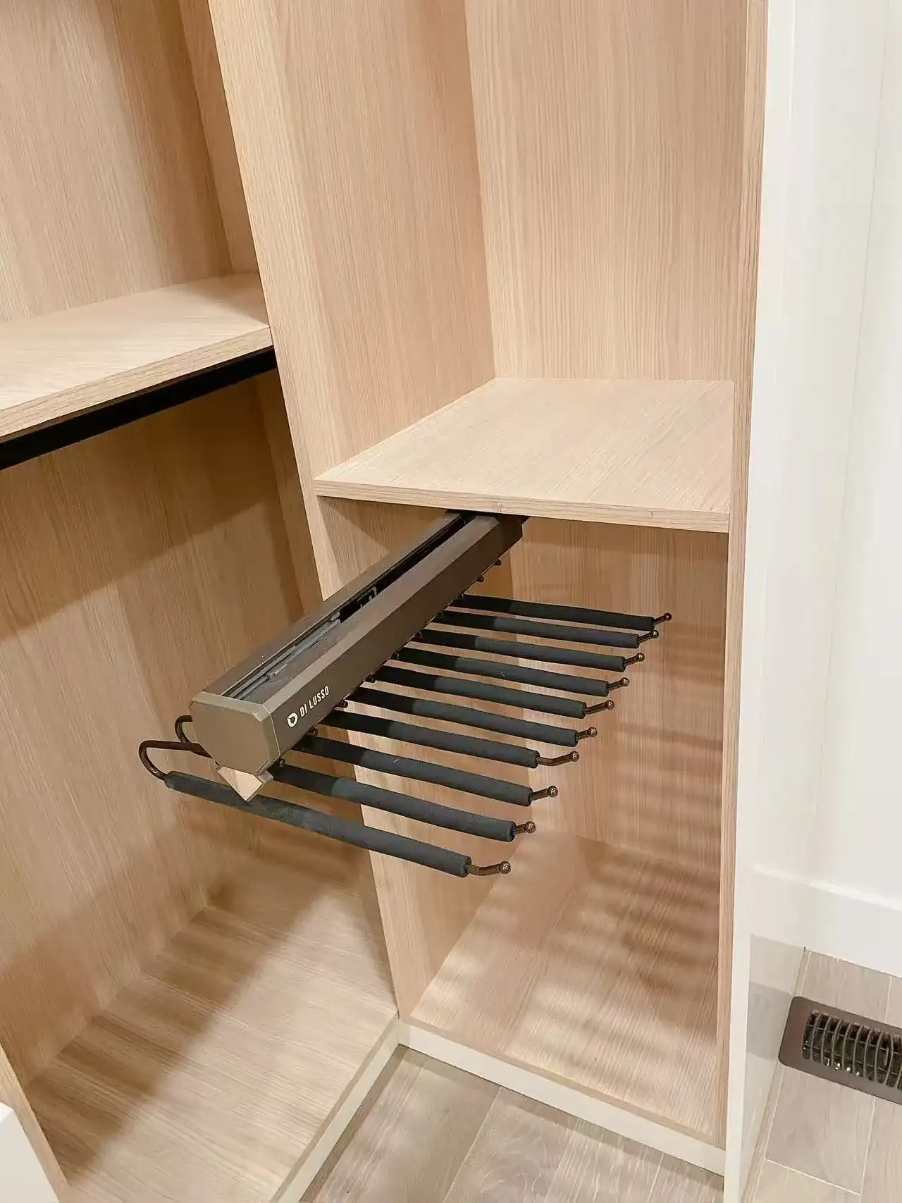 Pull-out pant rack with metal rails extended from a light wood closet section