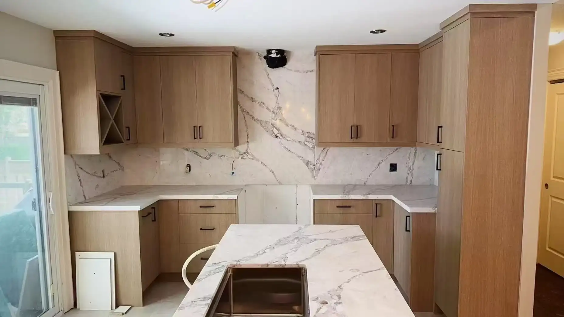 Newly installed wood kitchen cabinets and stone countertop, with outlets and wiring not yet connected