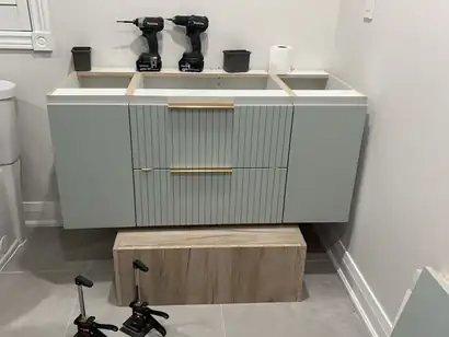 Sage green floating bathroom vanity with fluted drawer fronts and brass pulls being installed