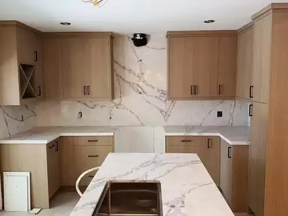 Wood-grain kitchen cabinets with a marble-look quartz backsplash and counters near completion