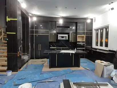 Black floor-to-ceiling kitchen cabinets with gold trim being installed beside an open staircase