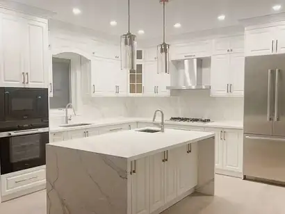 White shaker kitchen with a marble-look waterfall island, wall ovens and a stainless fridge