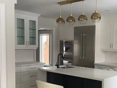 White kitchen with glass-front uppers, built-in ovens and a quartz island under gold pendants