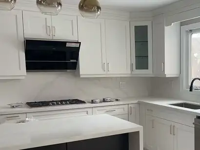 White shaker kitchen with a quartz waterfall island, gas cooktop and corner sink window
