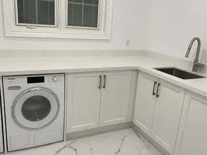 White laundry room cabinets with a quartz counter, sink and front-load washer and dryer