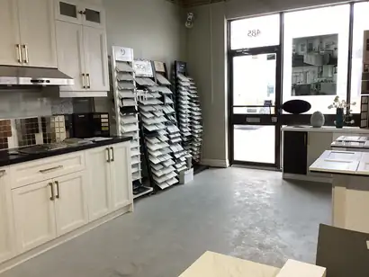 Showroom racks of cabinet door and countertop samples beside a white display kitchen