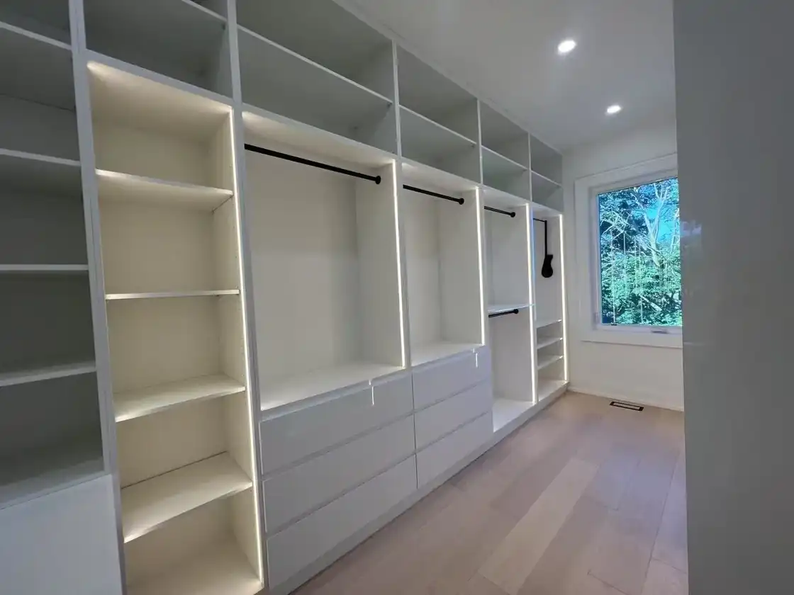 Walk-in closet with lit shelves, hanging rods and drawers along one wall and a clear walkway